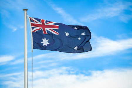 Australian flag flying on a flagpole with clouds and blue sky in the background