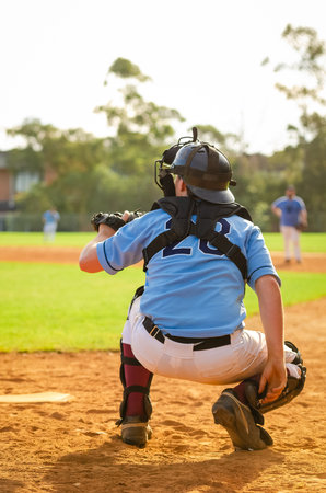 Men playing baseball game. Catcher is getting read to catch baseball during ballgame on a baseball diamond, field.の写真素材