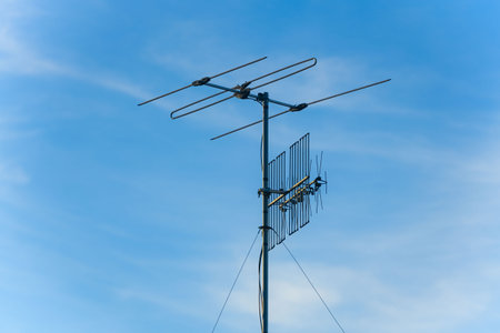 TV antenna mounted on a metal pole against a clear blue sky. Traditional rooftop aerial used for receiving digital and analog broadcast signals.の写真素材