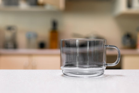Empty glass cup sitting on laminated kitchen benchtop, with cupboards and cooking appliances in background.の写真素材