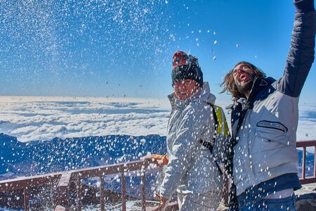 girl and boy having fun with snow in winter on top of the mountain with a blue background