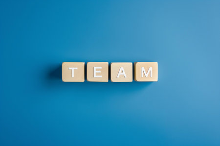 A minimalist image well-suited for business presentations, team-building workshop materials, or any medium emphasizing collaboration and group dynamics | This image presents a clean, straightforward message with the word 'TEAM' spelled out in block letters against a solid blue background. The choice of a bold, calming blue tone sets a professional tone and provides a contrasting backdrop that makes the beige tones of the wooden blocks stand out. The blocks are neatly aligned, suggesting order and unity, key elements of a successful team. The simplicity of the composition draws attention to the central theme without distraction, enabling the viewer to quickly grasp the concept of teamwork and collective effort. The casting of a soft shadow beneath each block adds depth to the image and subtly signifies the impact each team member has within the group. The sharp focus on the letters highlights their texture and emphasizes the building-block metaphor often associated with constructing a strong team foundation | Ideal for use in corporate training materials advocating for teamwork, as visual aids in leadership seminars, or as an encouraging print for office environments to inspire cooperation. The image's versatility allows for a range of applications, including website headers, social media posts, or brochure designs where a professional, yet approachable image is desired | a clean and concise photograph symbolizing the essence of teamwork through lettered blocks, set against a monochromatic blue background that provides a visually appealing contrast and space for additional text or design elementsの素材