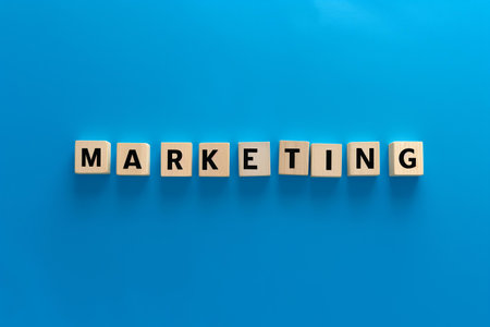A straightforward yet powerful image suitable for use in business presentations, marketing materials, or blog posts related to branding, advertising, and commerce | This image features the word "MARKETING" spelled out in bold, capital letters on wooden blocks, set against a solid, vibrant blue background. The minimalist design emphasizes clarity and focus, with the natural texture and grain of the wood juxtaposing the smoothness of the backdrop. The choice of a monochromatic blue color scheme evokes feelings of trust, intelligence, and communication, which are key elements in successful marketing strategies. The wooden blocks suggest building blocks, symbolizing the foundational and strategic aspects of marketing that companies use to construct their brand identity and market presence. The simplicity of the setup allows for direct conveyance of the image's core message, highlighting the essence of marketing in the business world | Ideal for educational content emphasizing the basics of marketing principles, as a visual accent in presentations that focus on the structure and building blocks of effective advertising, or as a cover image for marketing toolkits and guides. It also works well as a background for inspirational quotes about business growth, creativity in advertising, and the importance of a solid marketing plan | a clean and effective visual metonym for the concept of marketing, featuring wooden letter blocks spelling out 'MARKETING' on a singular blue background, offering a stark contrast and room for text or additional graphicsの素材