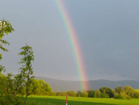 A massive rainbow over the village in the middle of a sunny day after the rain divides the sky into lighter and darker.のeditorial素材