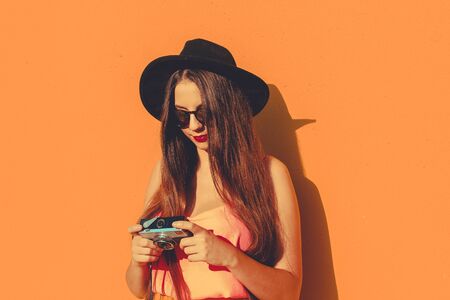 Girl using a vintage photo camera wearing fashionable sunglasses and a black hatの写真素材