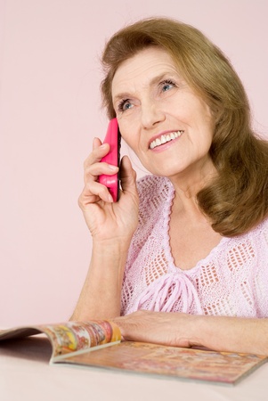 Pretty old woman with a phone on a pink backgroundの写真素材