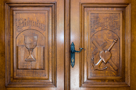 Novi Sad, Serbia - April 28, 2019: Wooden door with christian symbols: Bible, medieval cup, heart, cross and anchorのeditorial素材