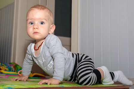 A nine-month-old boy with blond hair and blue eyes. Boy playing on the floor. Baby posing for a photographerの写真素材