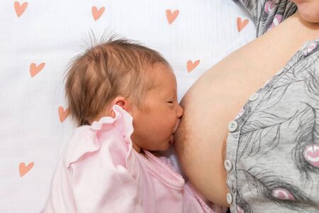 Close up mother breastfeeding her newborn child on a bed with a heart in a bright room. Mother...