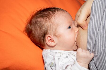Close up mother breastfeeding her newborn child on a bed with a heart in a bright room. Mother...