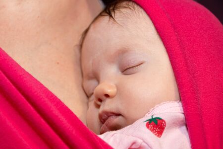 Baby is sleeping in sling, close up face. Newborn baby sleeping in a sling, in the embrace of her mother. The baby girl is 2 months old.の写真素材