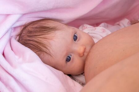 Mother breastfeeding her newborn baby. Baby is looking at the camera. The baby girl is two months...