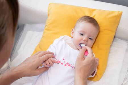 Cute little baby girl lying on the bed and eating rice soup with spoon. Mother feeding her baby girl. The baby girl is four months old.の写真素材