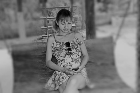 Ranong/ Thailand- 01.11.2018: Asian beautiful woman, wearing a lace drop skirt working on a mobile phone, sitting on a wooden chair surrounded by nature, mountains, trees, Thailandのeditorial素材