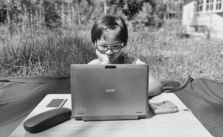 Ranong/ Thailand- 04.05.2020: Asian girl look at laptop learning from home with smartphone and camera in the front yard, process of self-study education for children, back to school concept.のeditorial素材