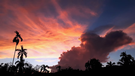 Create beauty of landscape saw mountains, betel palm coconut trees, with blue sky mix golden orange. the natural atmosphere evening is bright and charming in the countryside.の写真素材