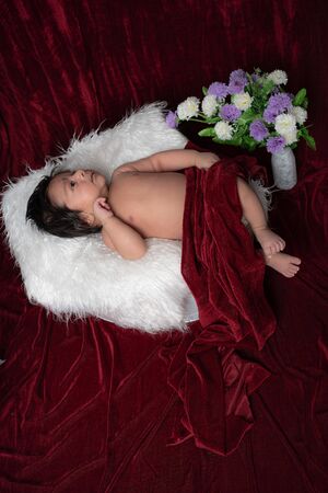 Adorable Baby Boy laying on White fur blanket and cover with red velvet blanket. Give pose like he is in deep thinking.の写真素材