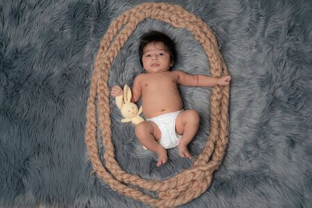 Portrait of a newborn baby boy, age 1 month, in a Diaper, Black hair, blue eyes on grey fur blanket holding a teddy bear and smiling. Family, love, children conceptの写真素材