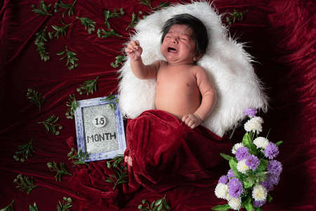 1.5 month baby boy crying while photo shoot rest on while pillow and covering with red velvet shawlの写真素材