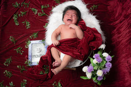 1.5 month baby boy crying while photo shoot rest on while pillow and covering with red velvet shawlの写真素材