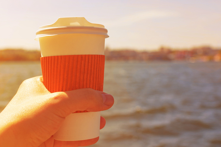 Coffee cup in hand against the backdrop of the lake at sunset.の写真素材