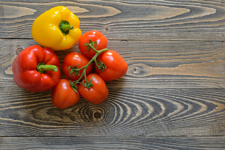 Five red tomatoes on a green branch and red pepper on a wooden background in the top left cornerの写真素材