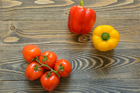 Five red tomatoes on a green branch and red pepper on a wooden background in the top left cornerの写真素材