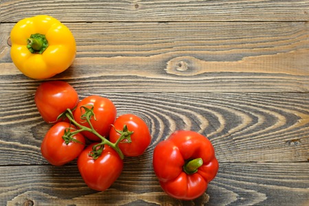 Five red tomatoes on a green branch and red pepper on a wooden backgroundの写真素材
