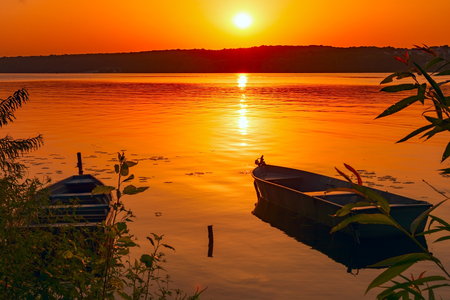 Two fishing boats moored near the shore of a pond against the background of the sunset. Toned.の写真素材