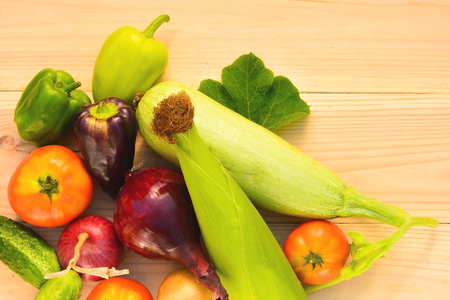 Green, purple peppers, tomatoes, corn, zucchini, blue and yellow onion on a wooden background in diffused lightの写真素材