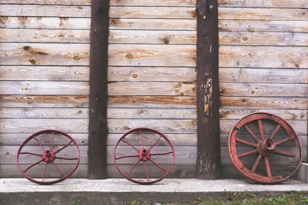 Three old wheels to a cart on the background of a wooden wooden tower wall on a concrete.の写真素材