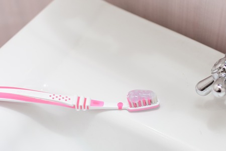 A pink toothbrush with a toothpaste is lying on the washbasin. Small depth of field.の写真素材