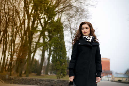 young beautiful happy girl in a coat posing at the parkの写真素材