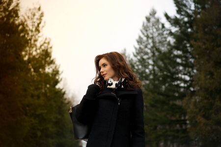 young beautiful happy girl in a coat posing at the park