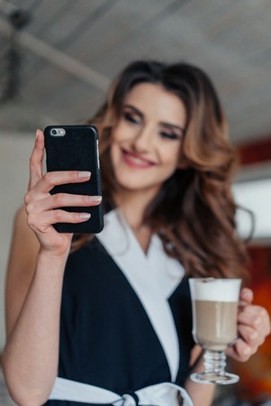 lady sitting at the table in cafe using phone and smiling.の写真素材