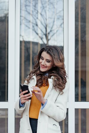 Girl walking and texting on the smart phone in the street wearing a red jacket in winterの写真素材