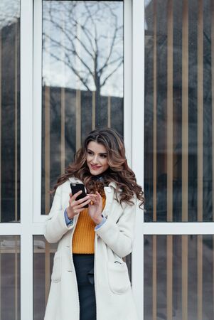 Girl walking and texting on the smart phone in the street wearing a red jacket in winterの写真素材