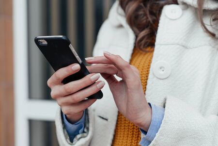 Girl walking and texting on the smart phone in the street wearing a red jacket in winterの写真素材