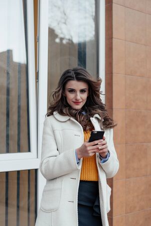 Girl walking and texting on the smart phone in the street wearing a red jacket in winterの写真素材