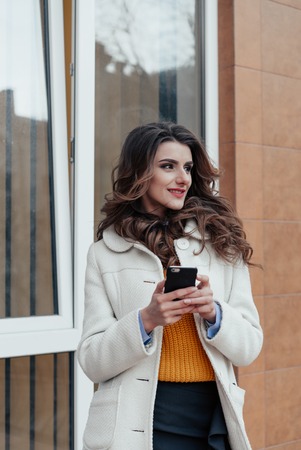 Girl walking and texting on the smart phone in the street wearing a red jacket in winterの写真素材