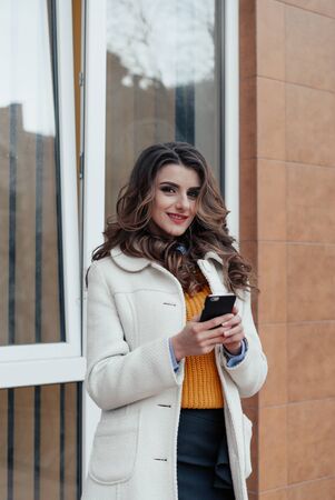 Girl walking and texting on the smart phone in the street wearing a red jacket in winterの写真素材