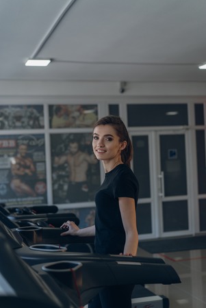 Woman posing for the camera on a treadmill in a fitness clubの写真素材
