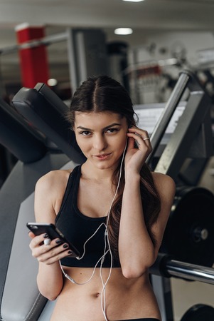 Young woman listening to music with earphones on smart phone app for fitness motivation. Athlete runner in sportswear relaxing sitting getting inspired.の写真素材