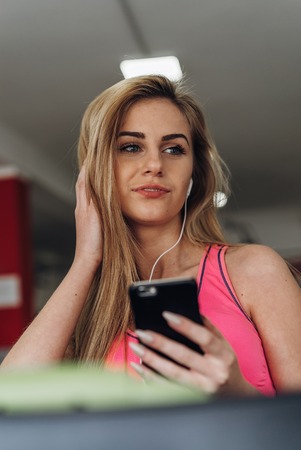 Young woman listening to music with earphones on smart phone app for fitness motivation. Athlete runner in sportswear relaxing sitting getting inspired.の写真素材