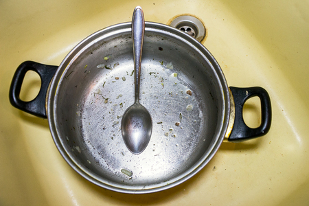 Unwashed pot with spoon is in the sinkの写真素材