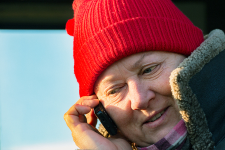 A woman in a warm coat and a red cap talking on the phoneの写真素材