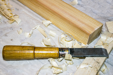 A chisel on the table among the shavings. Nearby there is a wooden bar. Selective focus
