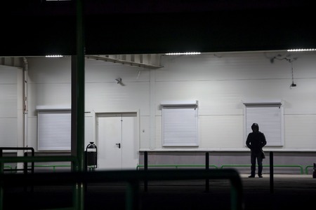 The guy in the hood stands at night under the lanterns near the white wall and is waiting for...