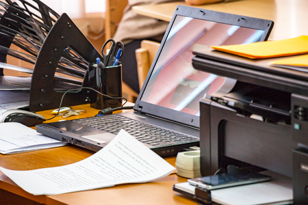 Office workplace with laptop, printer, stand for papers and business papers on the table