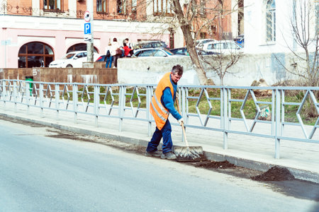 Russia, Samara, May 01, 2018: The janitor in an orange uniform cleans the garbage with a shovel on the city streetのeditorial素材